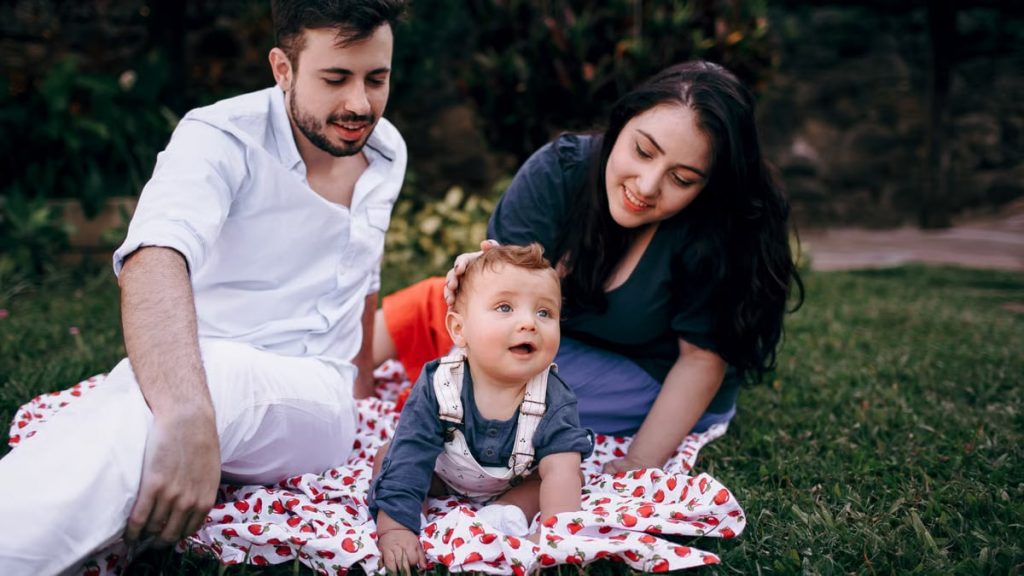 A joyful family enjoying a picnic outdoors during summer. Smiling parents with their baby on a blanket.